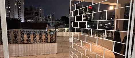 A balcony with a view of a cityscape at night, a tiled floor, and a white railing.