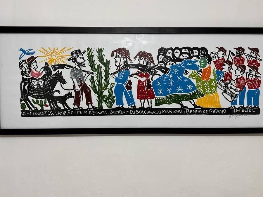 Una obra de arte enmarco que muestra a un grupo de personas vestidas con trajes tradicionales, con texto en la parte inferior.