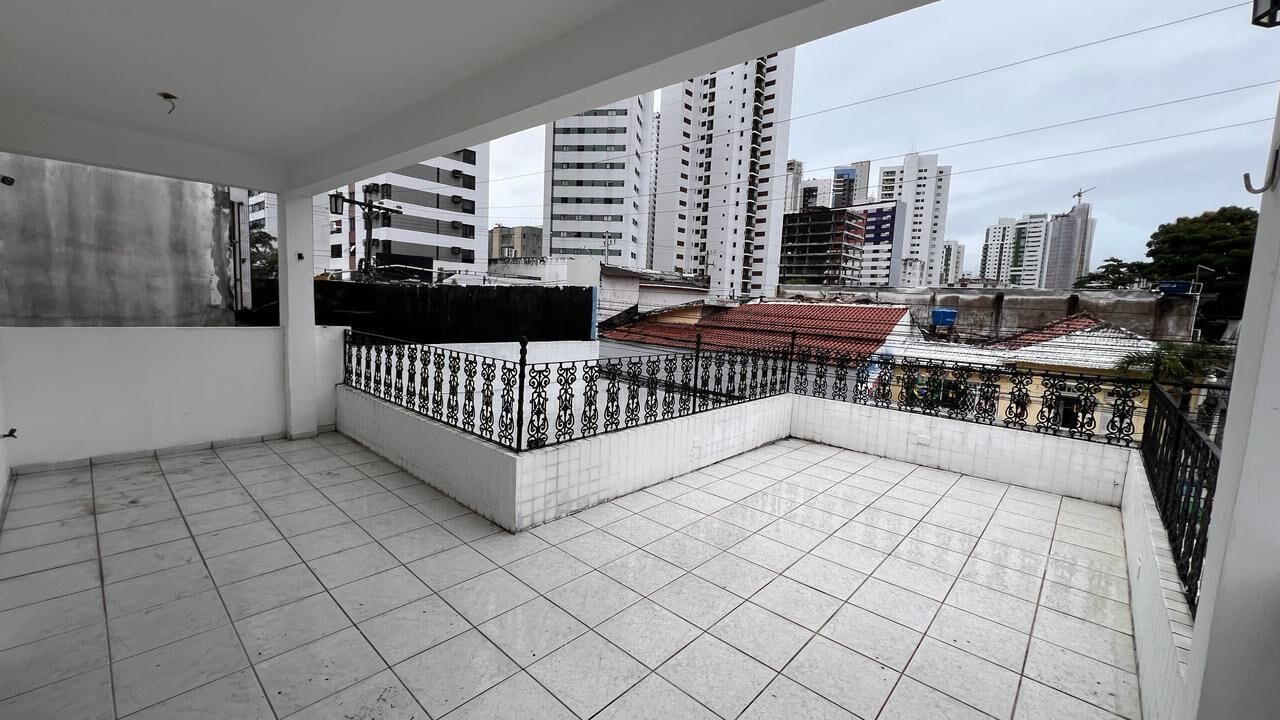Un balcón con suelo de baldosas, barandilla de metal negro y vistas de edificios altos.
