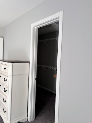 Ein Zimmer mit weißem Schminktisch, einem Kleiderschrank mit Kleiderstange und Teppichboden.