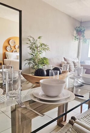 A dining area with a glass table, white plates, bowls, and a wooden bowl with decorative items. - Vista Tower, 3-bedroom apartment, panoramic view, rooftop pool and gym (San Salvador)