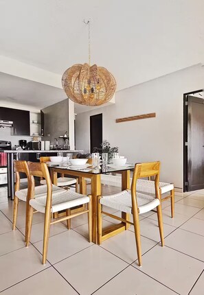 A dining area with a round table, four wooden chairs, and a woven pendant light. - Vista Tower, 3-bedroom apartment, panoramic view, rooftop pool and gym (San Salvador)
