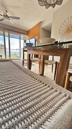 A room with a large window, a ceiling fan, a dining table with chairs, and a woven rug. - Vista Tower, 3-bedroom apartment, panoramic view, rooftop pool and gym (San Salvador)