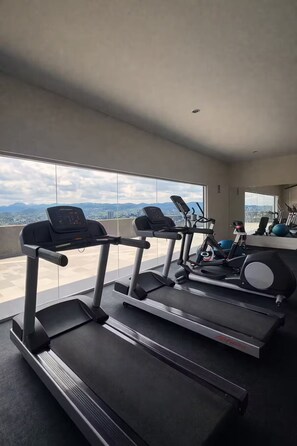 A gym with treadmills and exercise equipment, large windows with a city view. - Vista Tower, 3-bedroom apartment, panoramic view, rooftop pool and gym (San Salvador)