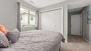 Ein Schlafzimmer mit Bett, Kleiderschrank, Fenster und einer Tür zu einem anderen Raum.