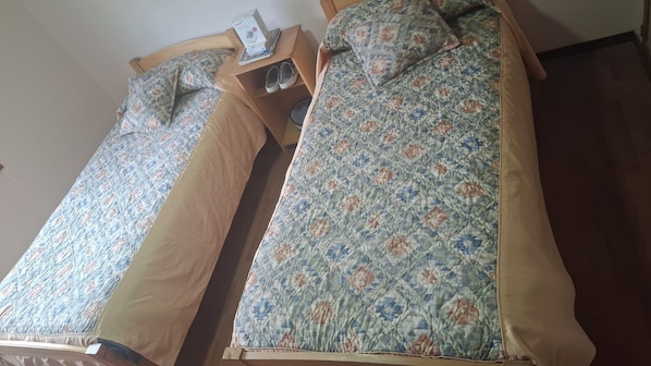 Two single beds with floral bedding, a wooden nightstand with a lamp, and a pair of shoes on the nightstand.
