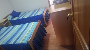 Quarto com duas camas, um guarda-roupa de madeira e uma mesa com cadeira.