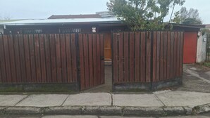 Ein durch einen Zaun gesichertes Gebäude mit einer Holztür, einer roten Wand und einem Metalldach.