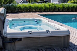 Ein Whirlpool auf einer Holzterrasse neben einem Schwimmbecken.