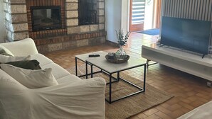 Ett vardagsrum med en öppen spis i sten, en vit soffa, ett soffbord och en tv som står på ett TV-bord.