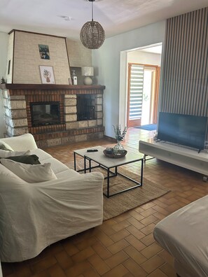 Ein Wohnzimmer mit Kamin aus Stein, einem weißen Sofa, einem Couchtisch und einem Fernseher auf einem Schrank.
