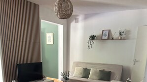 Ett vardagsrum med en soffa, en tv som står på ett tv-bord, ett soffbord och en hängande lampa.