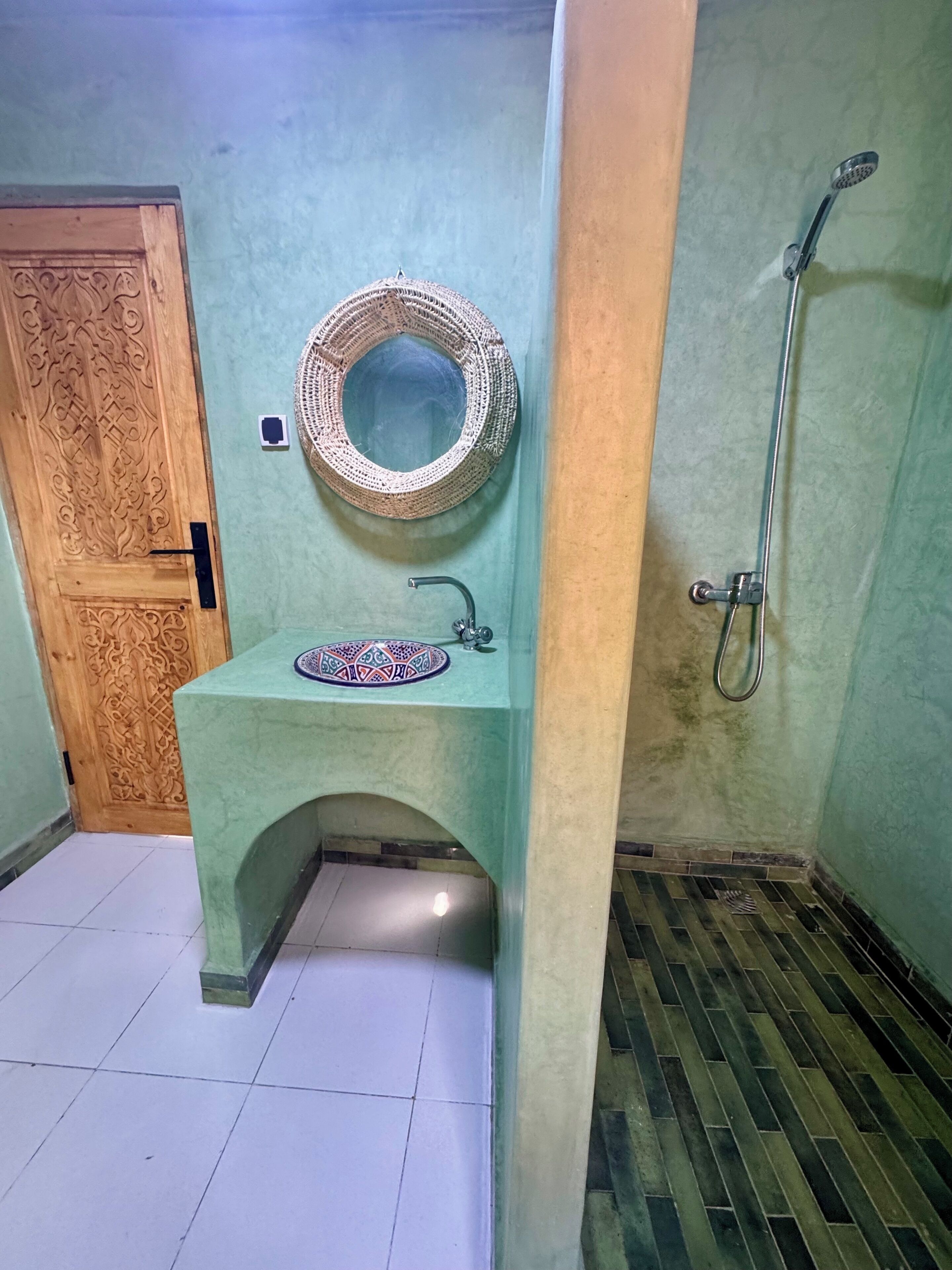 A bathroom with a wooden door, a sink with a decorative mirror, and a shower.