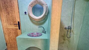 A bathroom with a wooden door, a sink with a decorative mirror, and a shower.