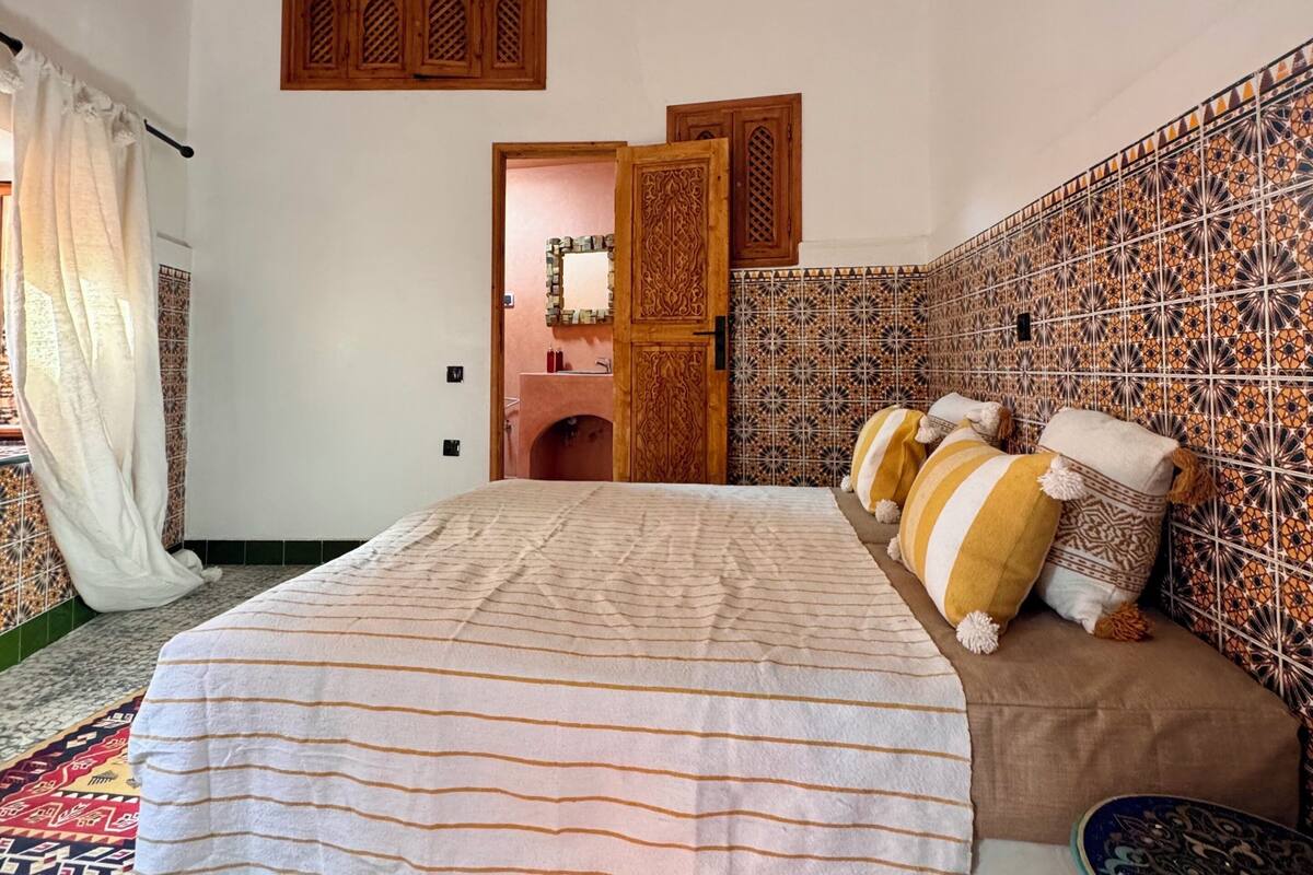Ein Schlafzimmer mit einem Bett, einem Schlafsofa, einer Wand mit Muster, einer Kristallleuchter und einer Tür zu einem anderen Raum.