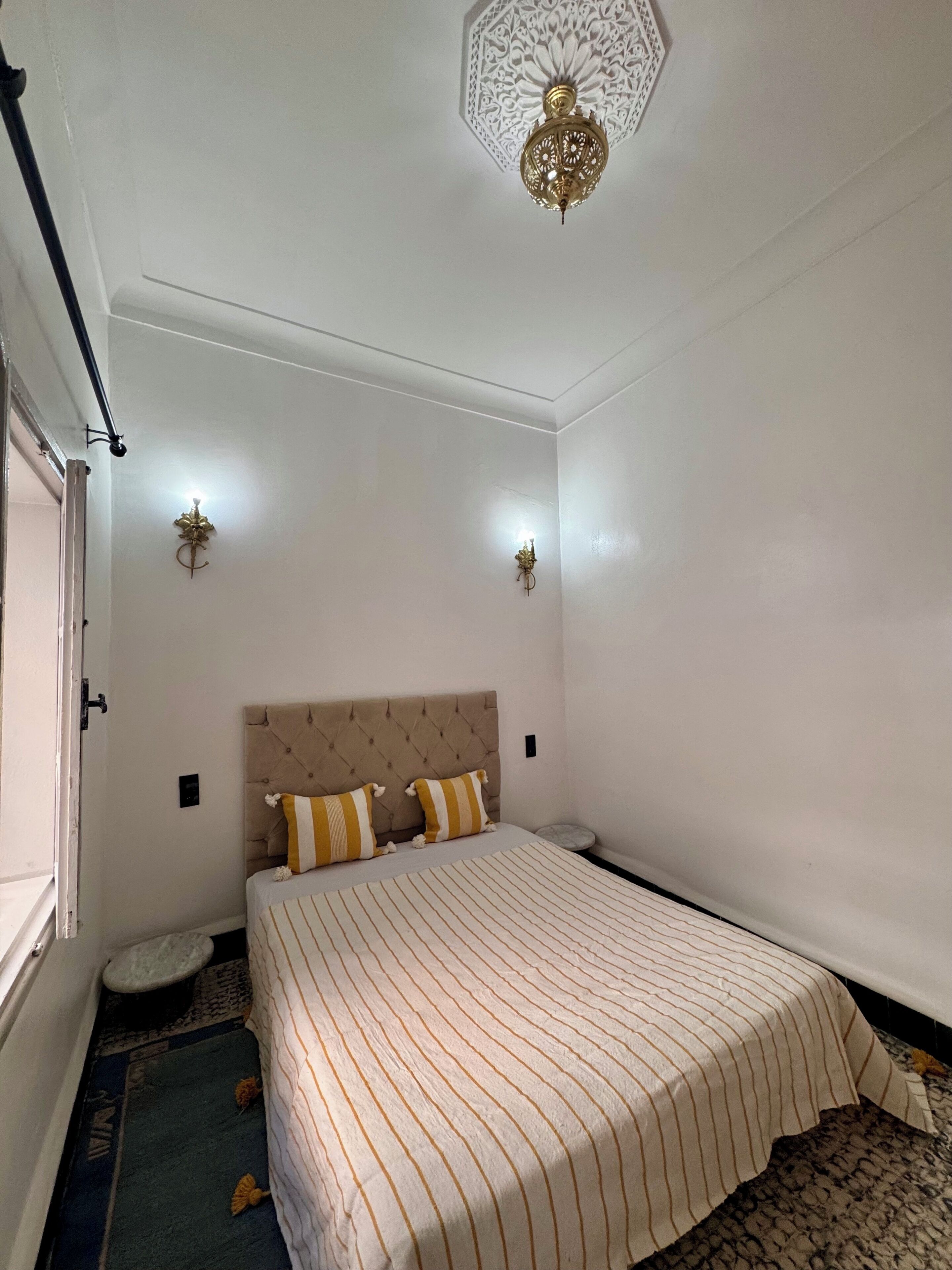Une chambre à coucher comprenant un lit, deux appliques murales, un luminaire décoratif au plafond et une fenêtre.