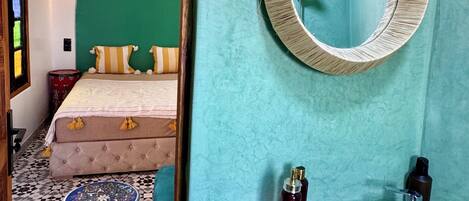 Une pièce comprenant un lit, un miroir rond, un lavabo décoré et un petit tabouret.