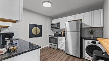 Una cucina moderna con mobili bianchi, elettrodomestici in acciaio inossidabile, un piano di lavoro in legno e un elemento decorativo nero e dorato.
