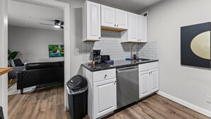 A compact kitchen with white cabinets, a dishwasher, and a black trash bin.