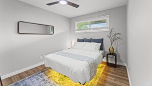 A bedroom with a bed, a ceiling fan, a window, a mirror, and a vase.