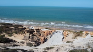 A coastal landscape with rocky terrain and a wooden walkway leading to a beach. - Beach Estates com Piscina Privativa By Carpediem (Aracati)