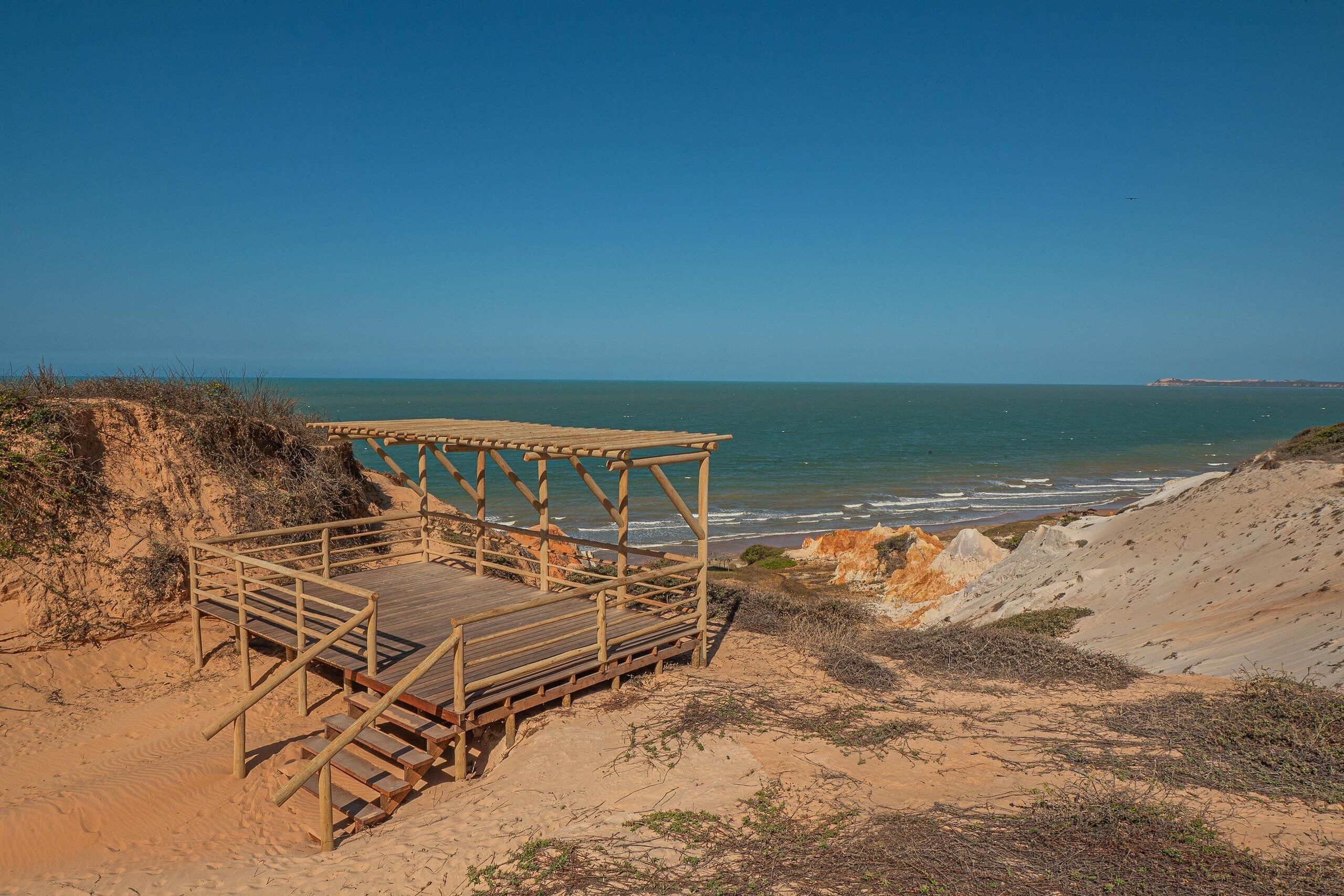 Una terraza de madera con vistas a una playa, bajo cielos despejados.