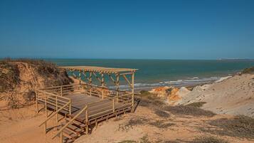 Una terraza de madera con vistas a una playa, bajo cielos despejados.