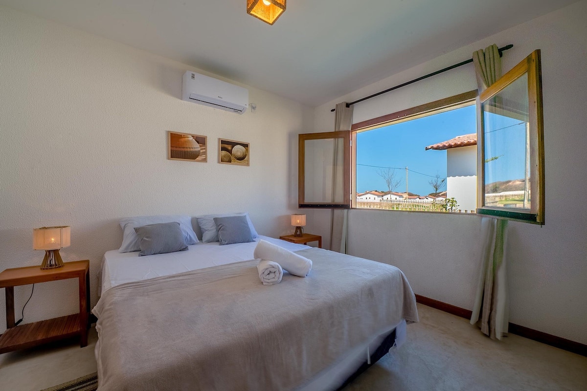 Habitación de hotel con cama, dos mesitas de noche con lámparas, aire acondicionado, ventana con vistas y cuadros en la pared.
