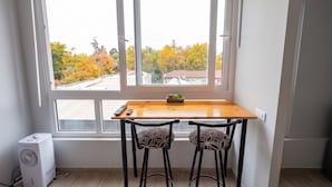 A room with a window, a wooden table, two chairs, a small plant, and a white air conditioner.
