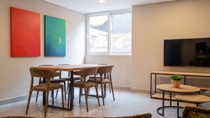 A modern living room with a dining area, a large window, and a flat-screen TV.