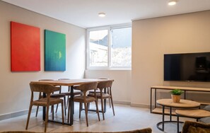 Una sala de estar moderna con comedor, un ventanal grande y un televisor de pantalla plana.