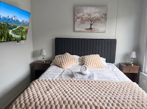 A neatly arranged bedroom with a bed, two bedside tables, a TV mounted on the wall, and a painting above the bed. - Movistar Arena - Metro Rondizzoni - Domus Travels (Santiago)