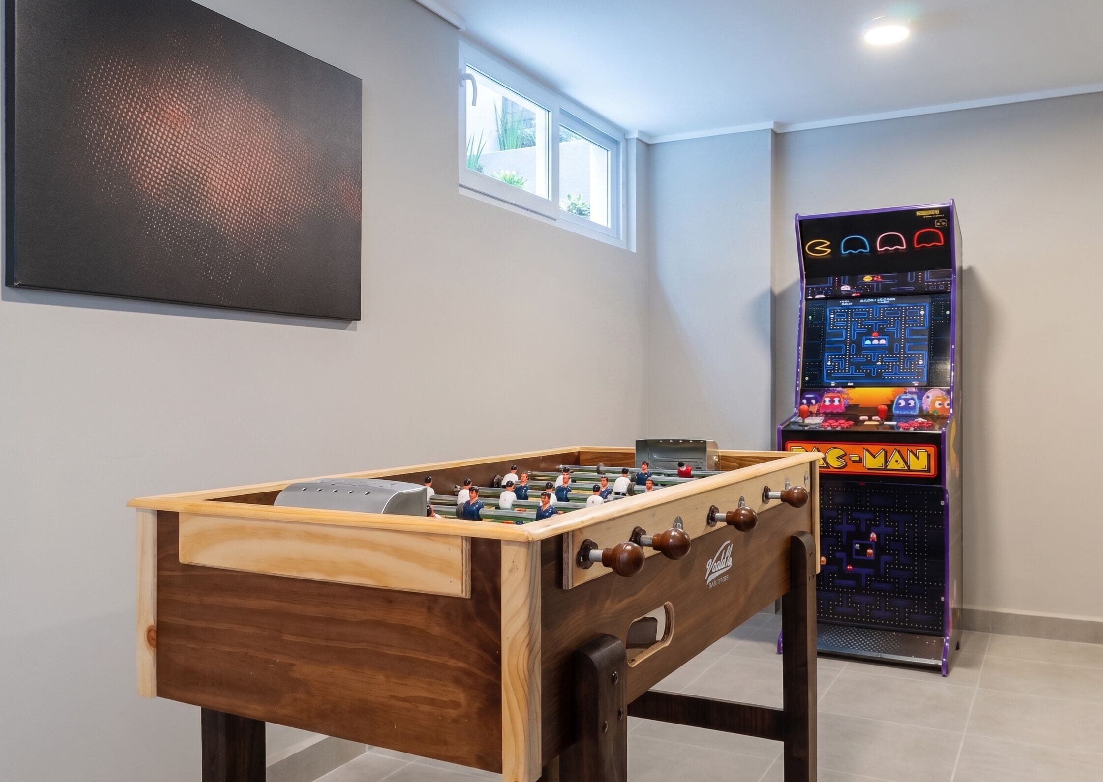 Une table de baby-foot et une console de jeux dans une pièce dotée d’une fenêtre et ornée d’une grande œuvre d’art au mur.