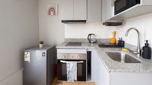 A compact kitchen with a refrigerator, oven, microwave, sink, and a clock on the wall. - Movistar Arena - Metro Rondizzoni - Domus Travels (Santiago)