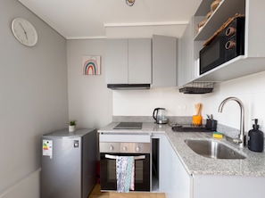 A compact kitchen with a refrigerator, oven, microwave, sink, and a clock on the wall. - Movistar Arena - Metro Rondizzoni - Domus Travels (Santiago)