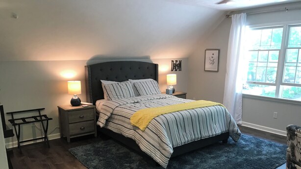 A bedroom with a bed, bedside tables, a nightstand, a chair, and a window with curtains.