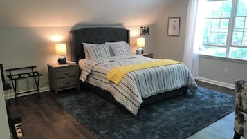 Un dormitorio con una cama, mesitas de noche, una silla y una ventana con cortinas.