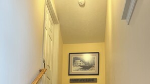 A wooden staircase with a handrail, a door at the top, a framed picture above a cabinet, and a 'Welcome Family & Friends' sign.