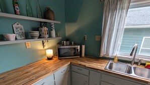 Uma cozinha com paredes verde-água, piso estampado, micro-ondas, pia e janela com cortinas.