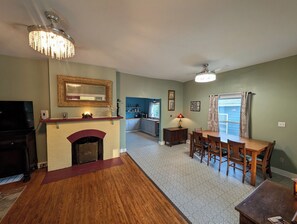Ein Wohnzimmer mit Kamin, Esstisch und einer Küche im Hintergrund.