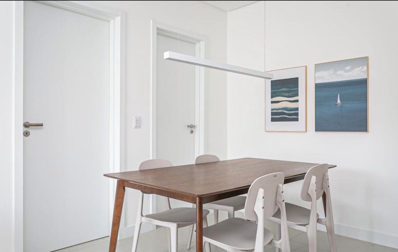 Une pièce avec une table en bois et des chaises blanches, une porte blanche et deux tableaux encadrés au mur.