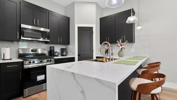 Una cocina moderna con armarios oscuros, electrodomésticos de acero inoxidable, una isla de mármol y taburetes de madera.