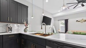 Una cocina moderna con armarios oscuros, lavavajillas de acero inoxidable e iluminación colgante.