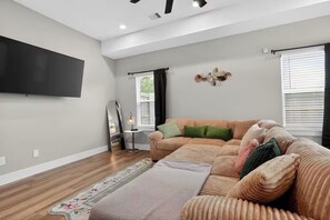Ein Wohnzimmer mit einer Couch, einem Flachbildfernseher, einer Lampe und einem Fenster mit Jalousien.