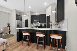 Eine moderne Küche mit dunklen Schränken, einer weißen Arbeitsplatte und drei Holzbarhocker.