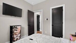 Un dormitorio con una cama, un televisor montado en la pared, un armario con obras de arte y dos puertas.