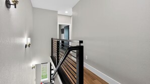 Una escalera moderna con barandilla negra, pared de gris claro y una ventana en la parte inferior.
