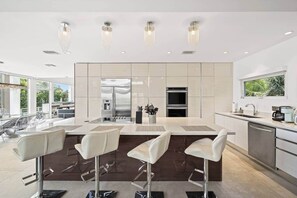 A modern kitchen with a central island, bar stools, stainless steel appliances, and pendant lighting. - Luxurious Retreat At The Whispering Palms (Wabasso Beach)
