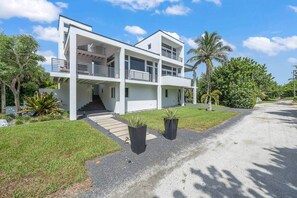 A modern two-story house with a balcony, a staircase leading to the entrance, and a well-maintained lawn with palm trees. - Luxurious Retreat At The Whispering Palms (Wabasso Beach)