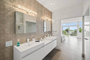 A modern bathroom with a large mirror, a white vanity, and a view of a balcony. - Luxurious Retreat At The Whispering Palms (Wabasso Beach)